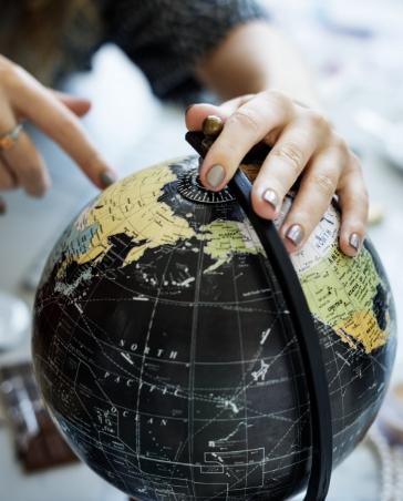 Hand zeigt auf einen schwarzen Globus, Symbol für internationale Ausrichtung oder globale Planung.